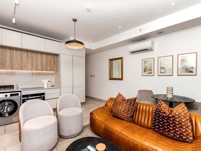 Modern open-plan living area featuring a sleek, integrated kitchen with built-in appliances, tiled flooring, and a wall-mounted air conditioning unit.