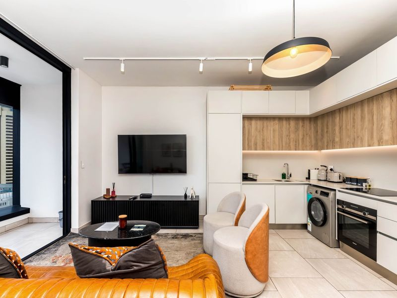 Modern open-plan living area featuring a sleek kitchen with integrated appliances, track lighting, and large sliding doors leading to a balcony.