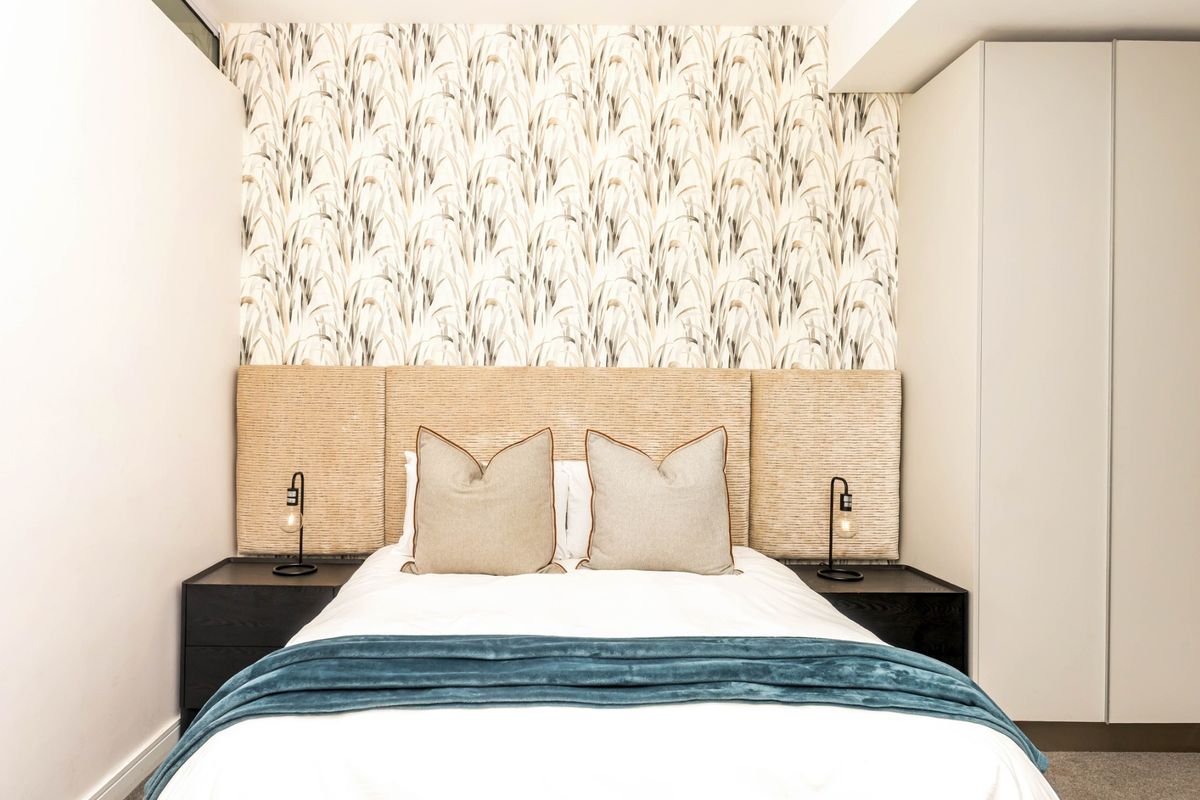 A well-appointed bedroom featuring a custom upholstered headboard, decorative feature wallpaper, and integrated built-in wardrobe storage.