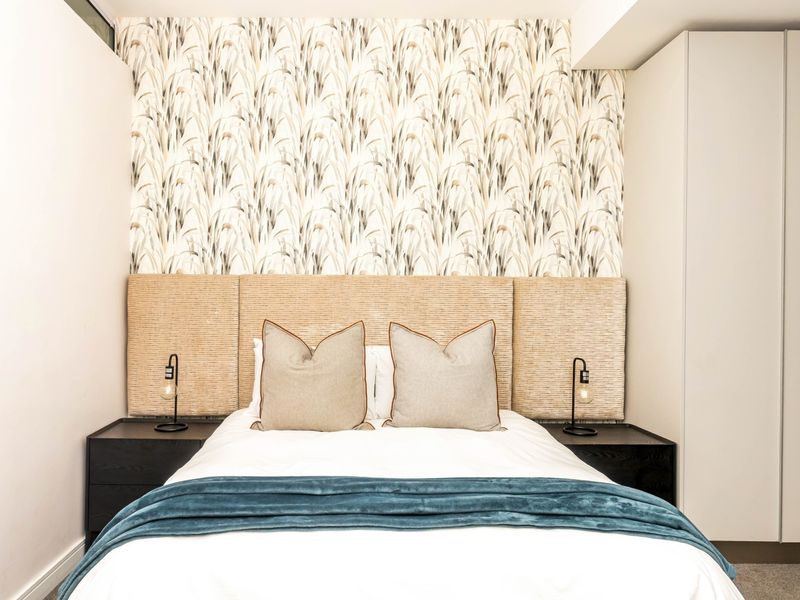 A well-appointed bedroom featuring a custom upholstered headboard, decorative feature wallpaper, and integrated built-in wardrobe storage.
