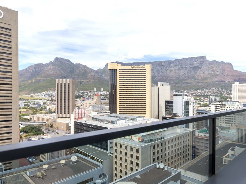 Elevated city view overlooking the urban skyline with Table Mountain in the background, framed by a modern glass balustrade.