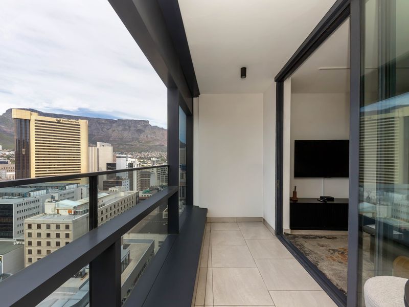 A modern, covered balcony featuring tiled flooring, a sleek glass balustrade, and expansive city and mountain views.
