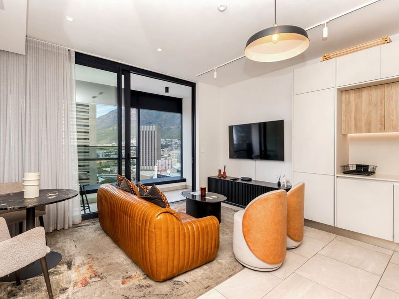 Modern open-plan living area featuring sleek built-in cabinetry, tiled floors, and large sliding glass doors opening to a balcony with city and mountain views.