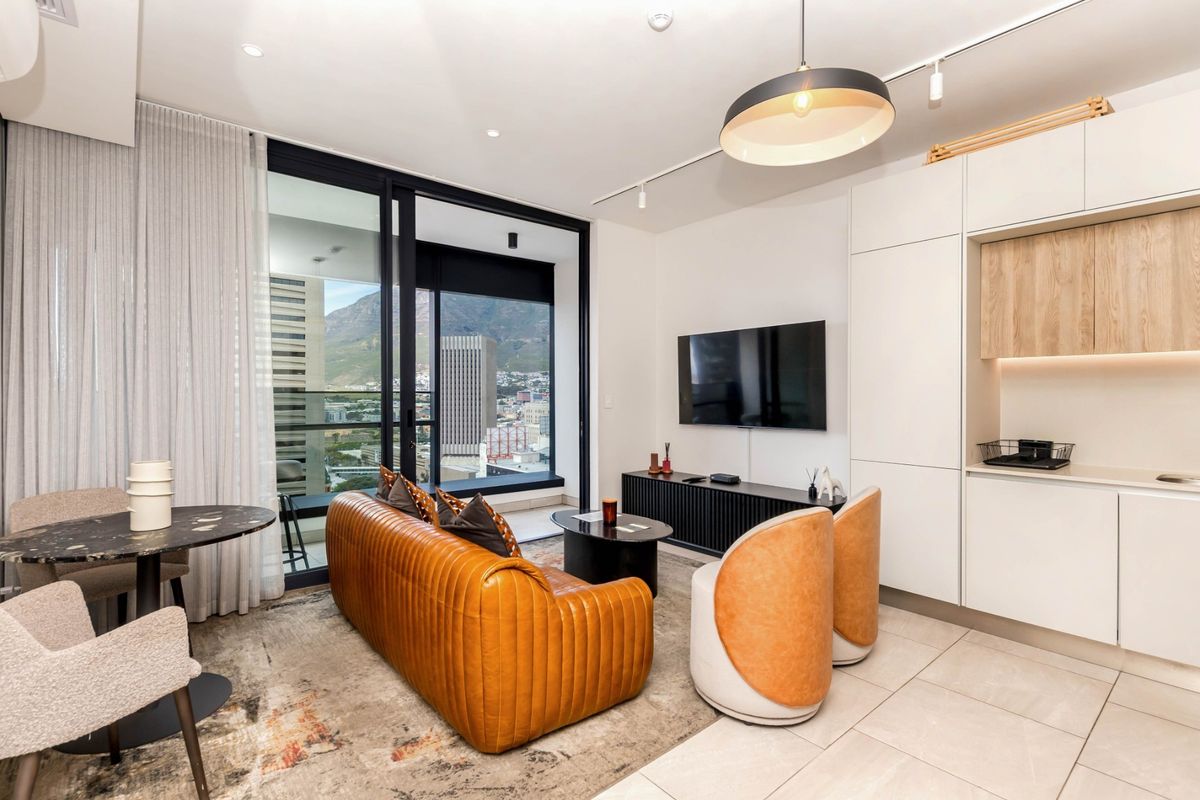 Modern open-plan living area featuring sleek built-in cabinetry, tiled floors, and large sliding glass doors opening to a balcony with city and mountain views.