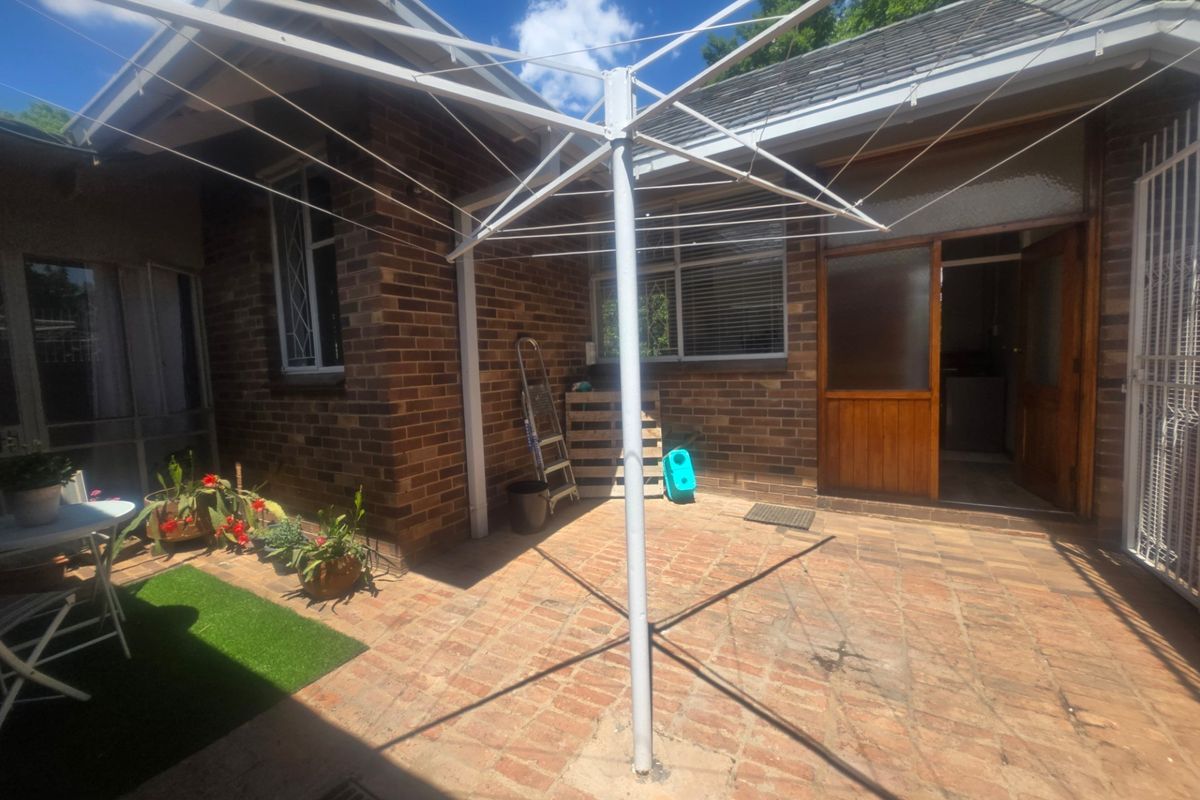A rear courtyard area featuring brick paving, a rotary clothesline, and direct access to the home through a timber-framed door.