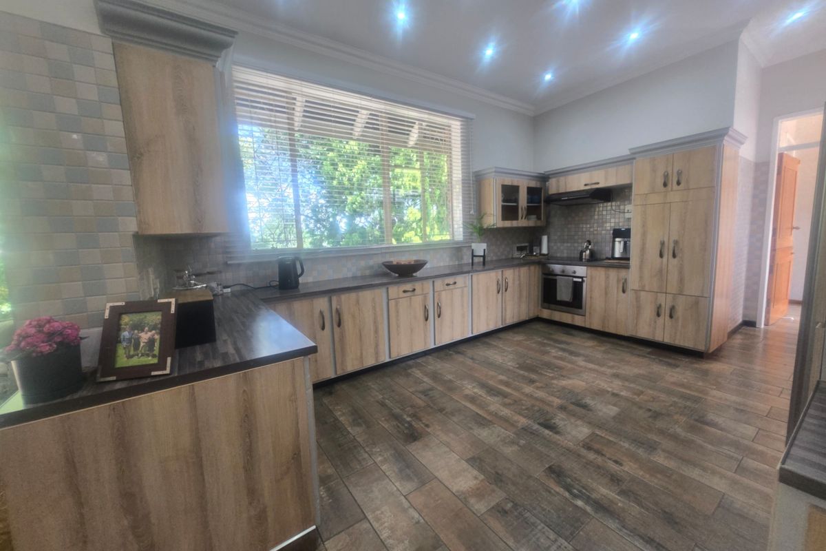 A well-maintained kitchen featuring wood-look cabinetry, dark laminate countertops, integrated oven, extractor fan, and modern wood-look floor tiles with ample natural light.
