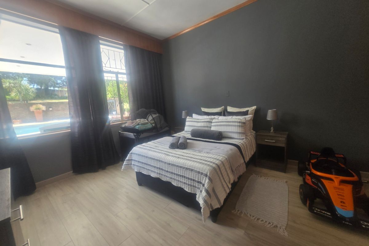 A well-lit bedroom featuring modern laminate flooring, dark accent walls, and large windows providing natural light and a view of the outdoor pool area.