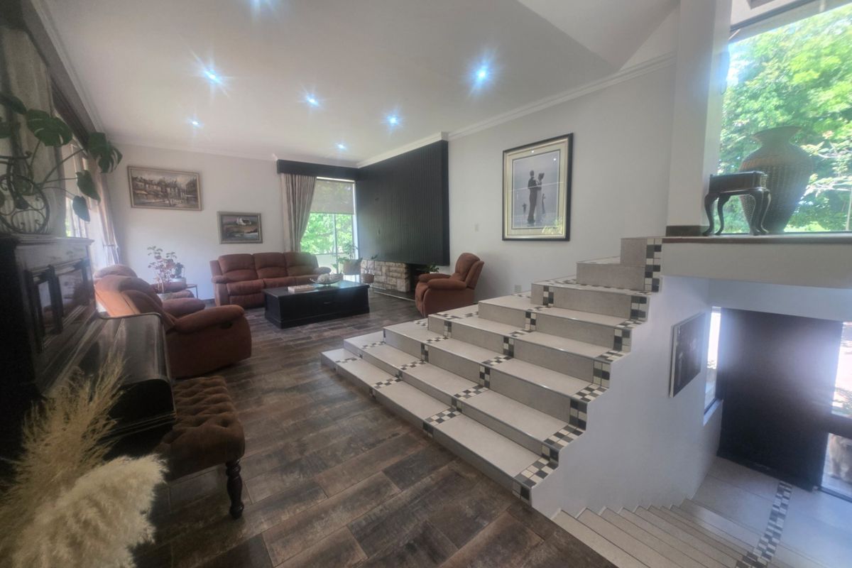 Spacious living room featuring wood-look floor tiles, a prominent tiled staircase, and a fireplace with decorative wall paneling.