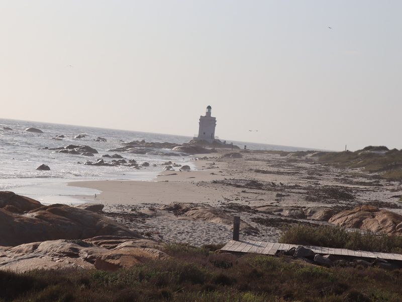 A scenic coastal view featuring a lighthouse situated on a rocky shoreline with sandy beach access.