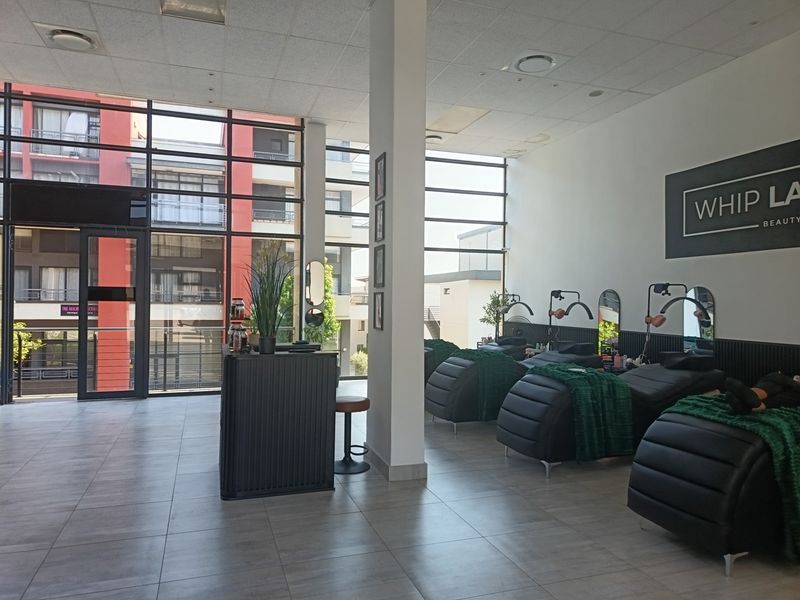 A bright, open-plan retail space featuring large floor-to-ceiling windows, tiled flooring, and a modern suspended ceiling, currently configured for beauty services.