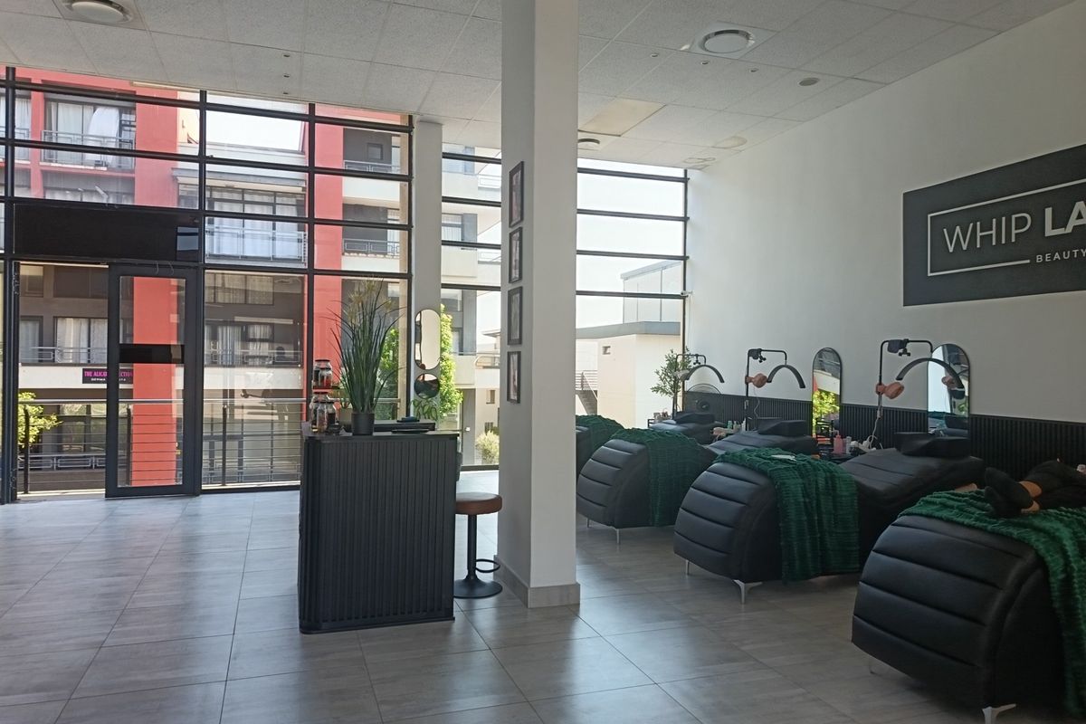 A bright, open-plan retail space featuring large floor-to-ceiling windows, tiled flooring, and a modern suspended ceiling, currently configured for beauty services.