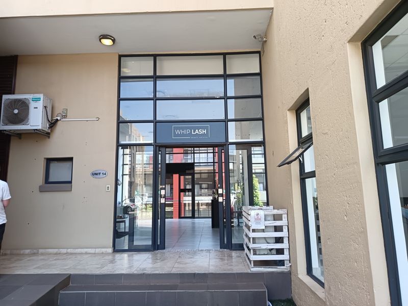 Front entrance of a retail unit featuring a glass facade, tiled steps, and exterior mounted air conditioning unit.