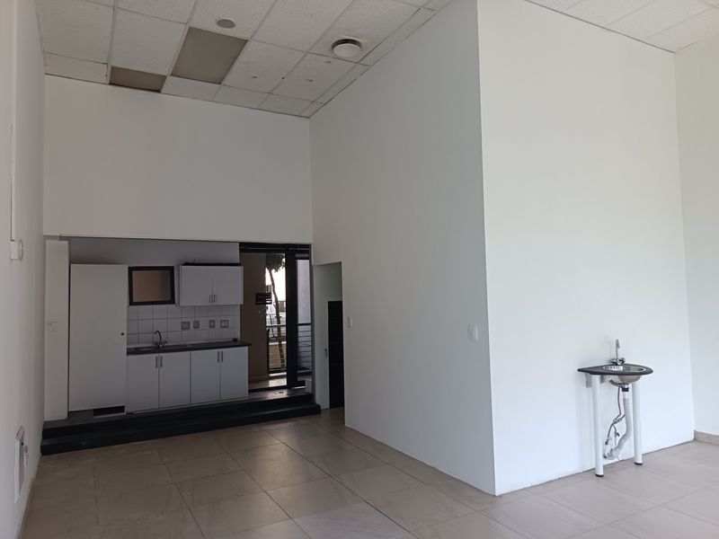 Open plan retail space featuring a kitchenette with built-in cabinetry, a stainless steel sink, and an additional pedestal sink area with tiled flooring.