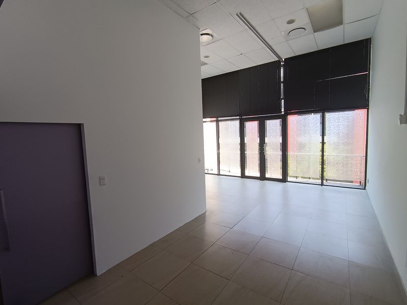Spacious open-plan retail or office area featuring large glass doors, tiled flooring, and a suspended ceiling, offering a versatile layout for various business needs.