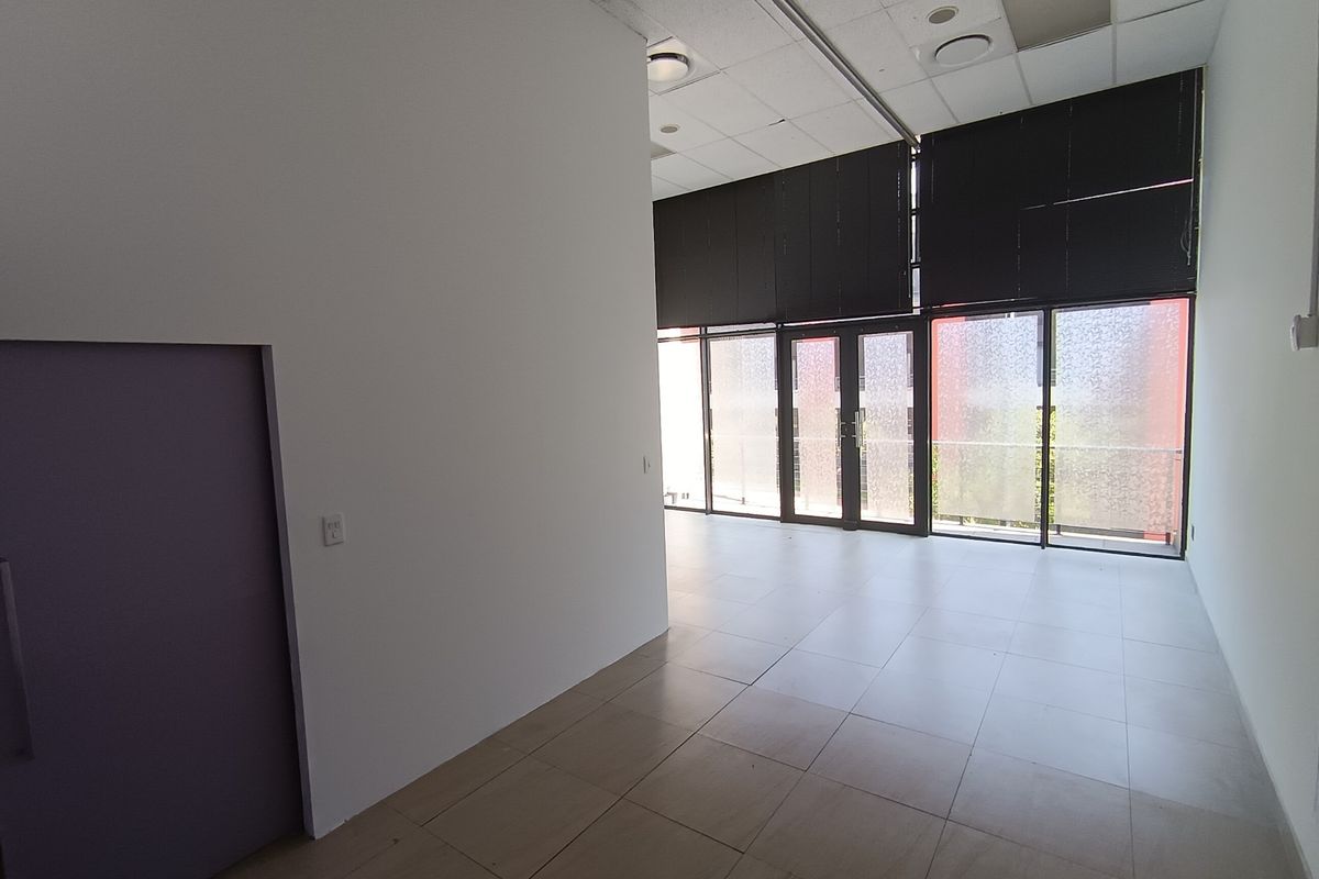Spacious open-plan retail or office area featuring large glass doors, tiled flooring, and a suspended ceiling, offering a versatile layout for various business needs.