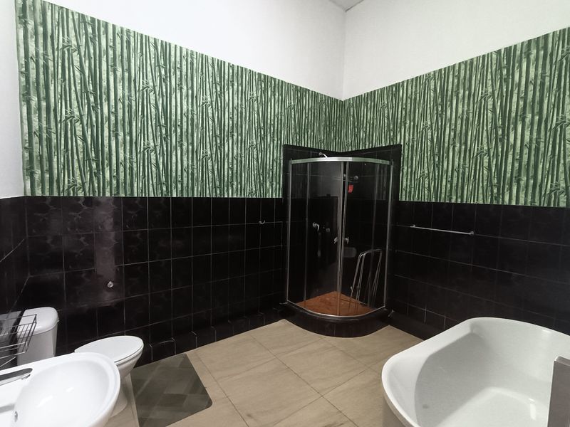 Bathroom featuring a corner shower enclosure, freestanding bathtub, pedestal sink, and toilet, finished with dark wall tiles and bamboo-patterned wallpaper.