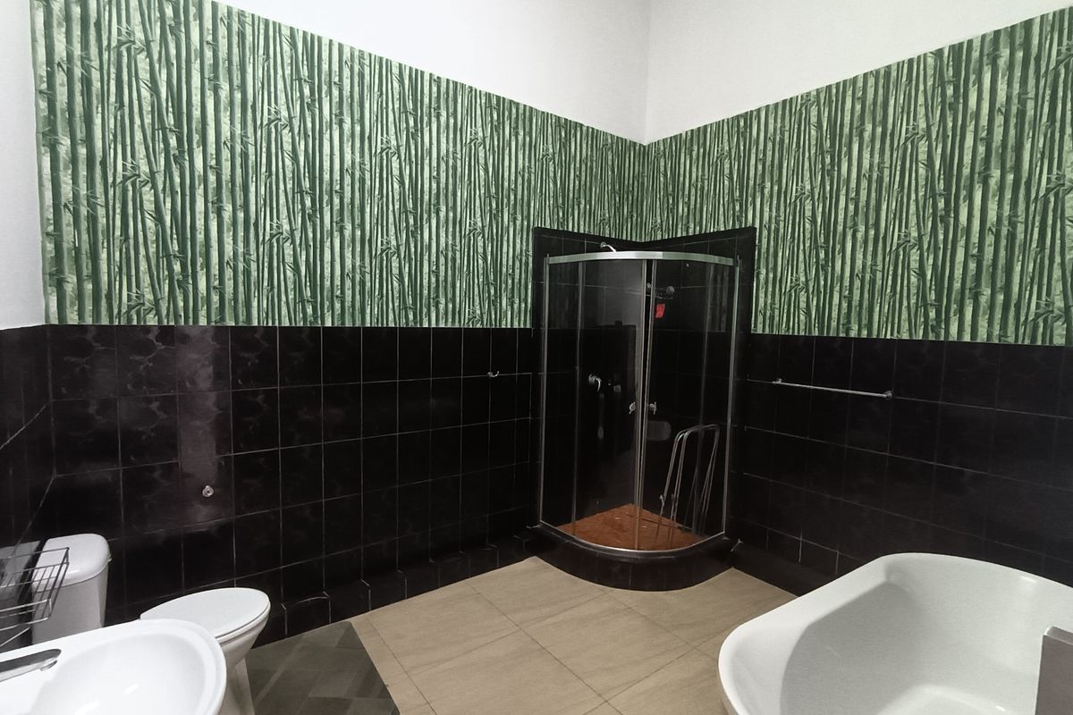 Bathroom featuring a corner shower enclosure, freestanding bathtub, pedestal sink, and toilet, finished with dark wall tiles and bamboo-patterned wallpaper.