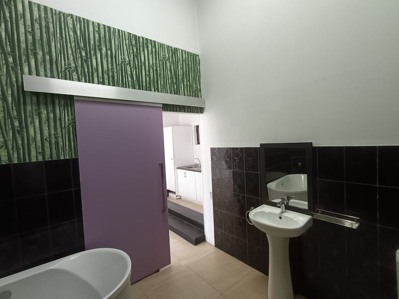A bathroom featuring a pedestal basin, dark tiled walls, and a sliding door leading to an adjacent utility area.