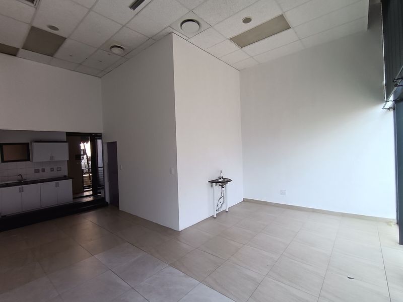 Open-plan retail space featuring tiled flooring, a suspended ceiling with recessed lighting, and a small kitchenette area with built-in cabinetry and sink.