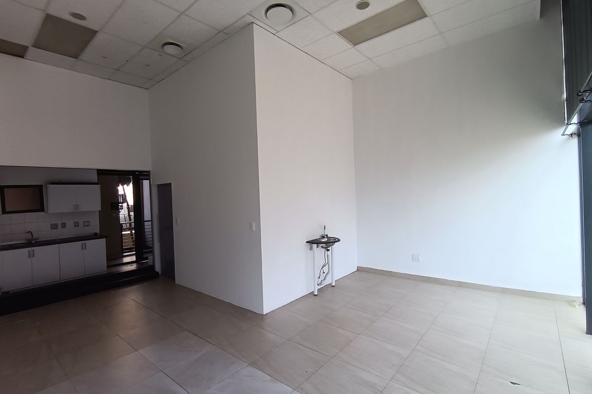 Open-plan retail space featuring tiled flooring, a suspended ceiling with recessed lighting, and a small kitchenette area with built-in cabinetry and sink.