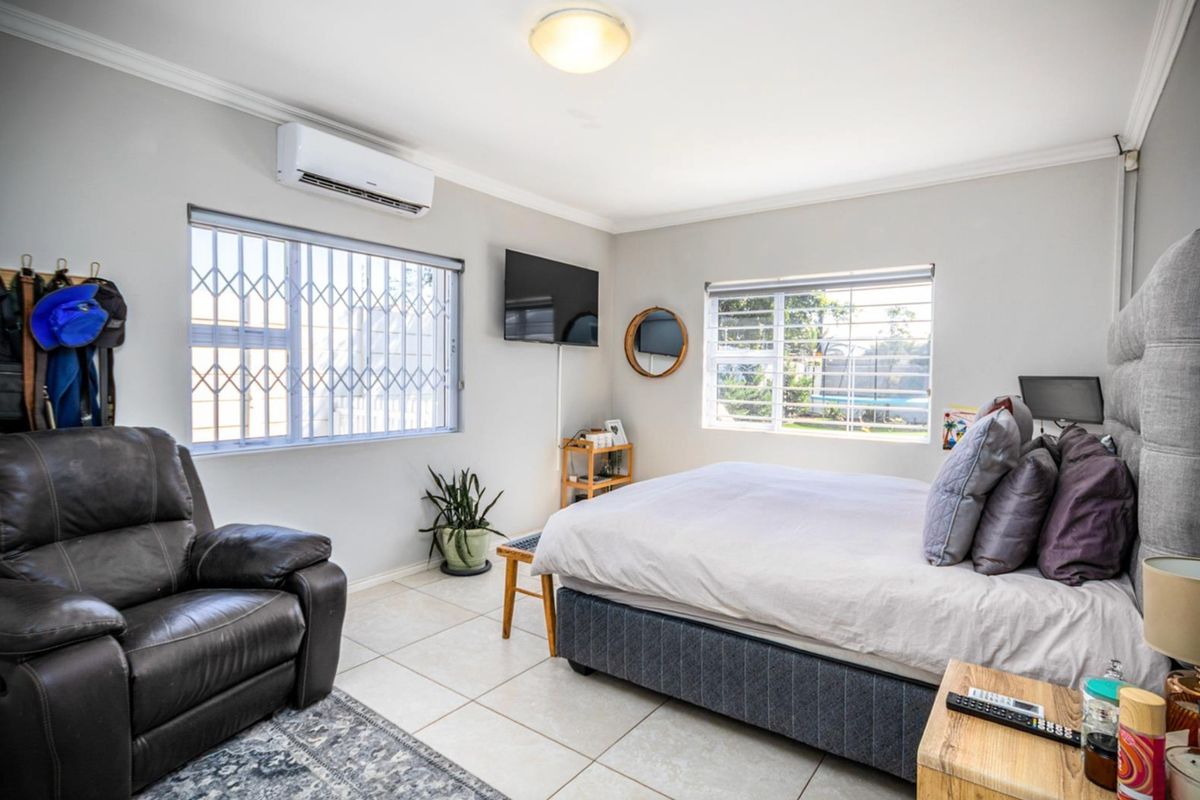 A well-lit bedroom featuring tiled flooring, security bars on windows, and a wall-mounted air conditioning unit.