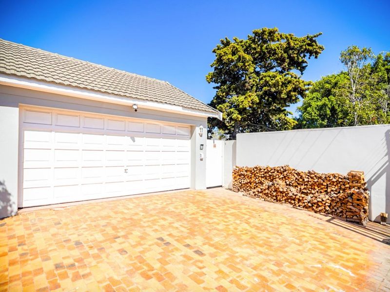 A well-maintained garage exterior featuring a white sectional door, tiled roof, and a neat brick-paved driveway area.