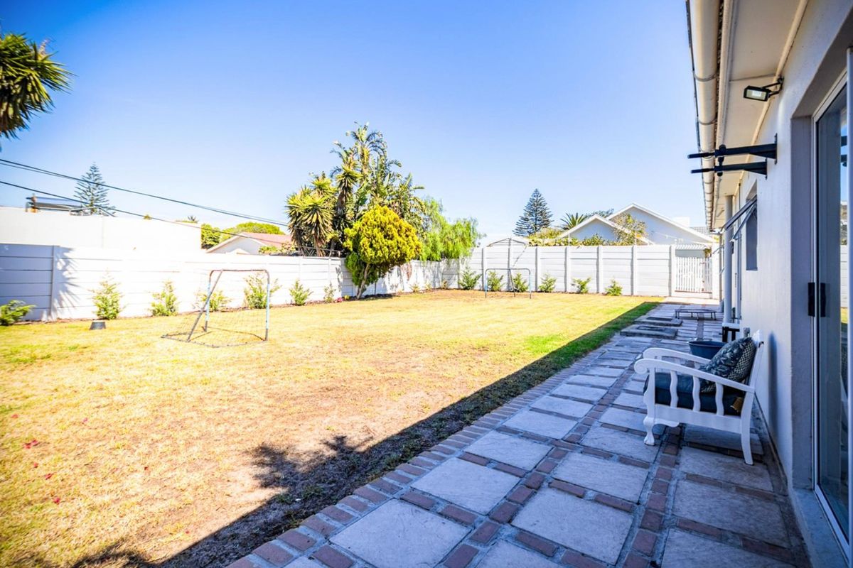 A spacious rear garden featuring a paved patio area, a large lawn, and secure perimeter boundary walls.