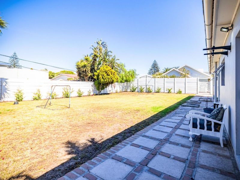 A spacious rear garden featuring a paved patio area, a large lawn, and secure perimeter boundary walls.