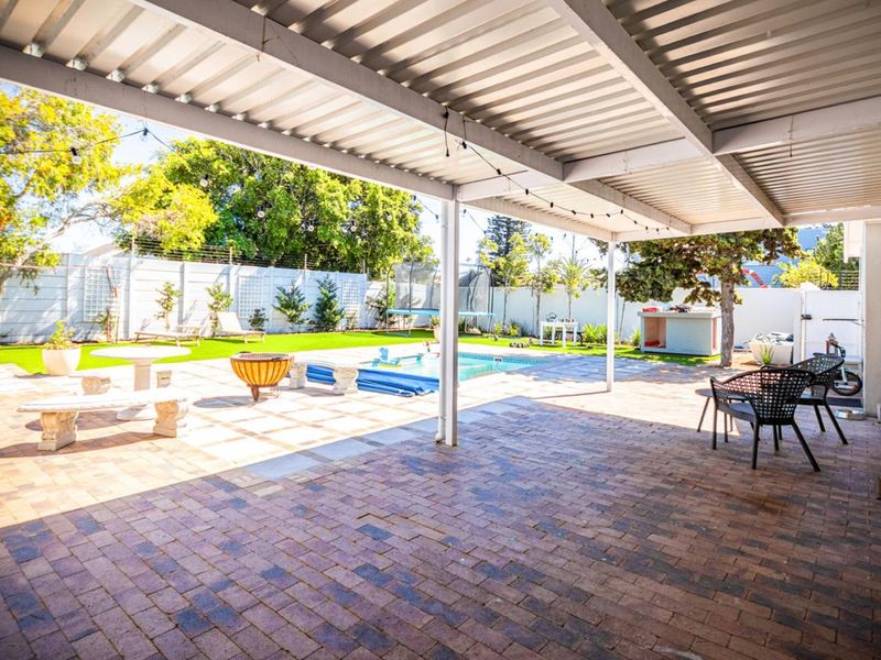 Spacious covered patio featuring paved flooring, overlooking a private swimming pool and a well-maintained garden area with secure boundary walls.