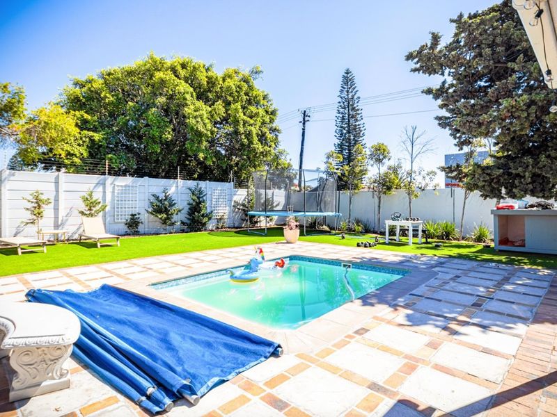 Outdoor pool area featuring a swimming pool, paved patio surround, and artificial lawn, enclosed by a perimeter wall with electric fencing.
