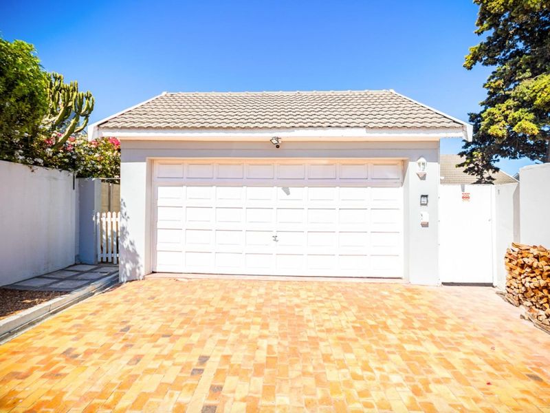 A well-maintained detached garage featuring a white sectional door, tiled roof, and a neat brick-paved driveway.