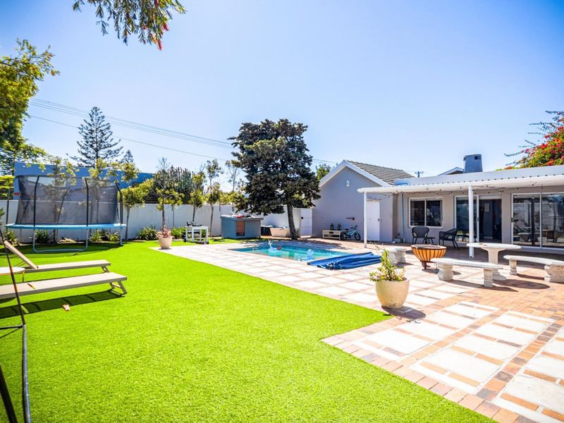 Spacious outdoor entertainment area featuring a swimming pool, paved patio, and artificial lawn, perfect for family gatherings and outdoor living.