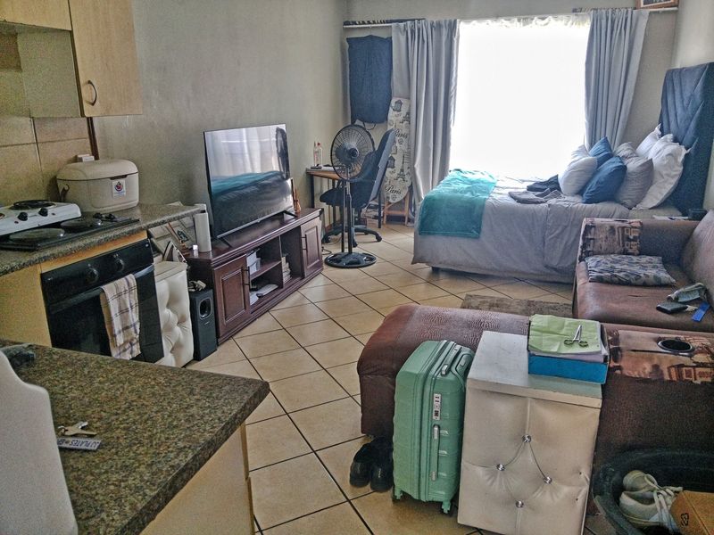 An open-plan studio apartment featuring a compact kitchen with built-in cabinetry and granite countertops, seamlessly flowing into the combined living and sleeping area.