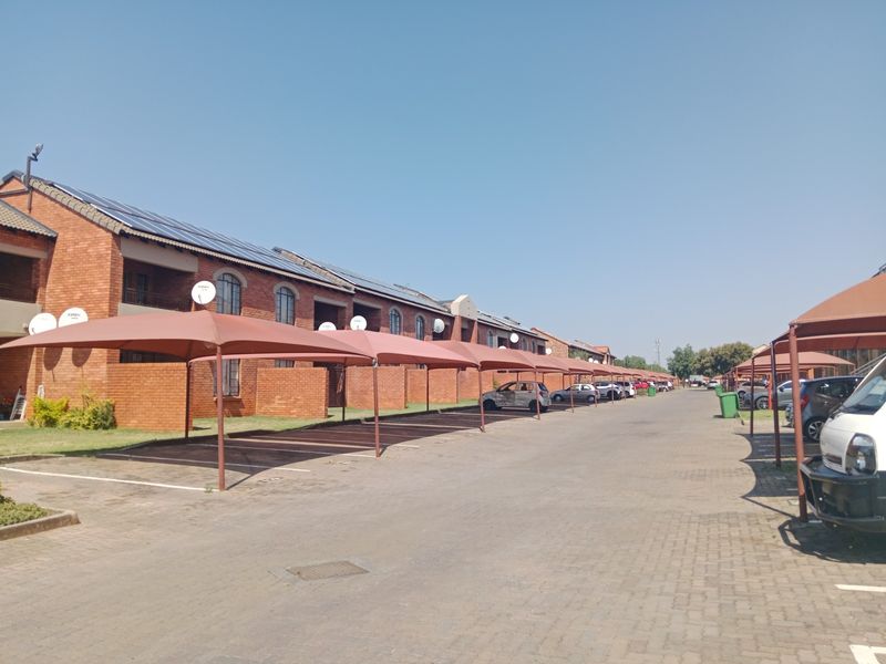 Exterior view of an apartment complex featuring brick facades, solar panels, and a long row of covered parking bays.