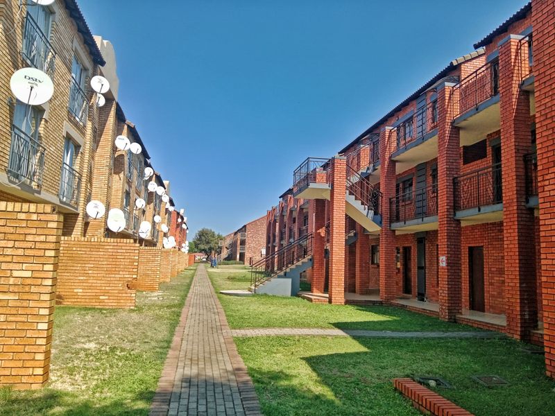 Exterior view of a multi-story apartment complex featuring face brick construction, external staircases, balconies, and a central paved walkway through a communal garden area.