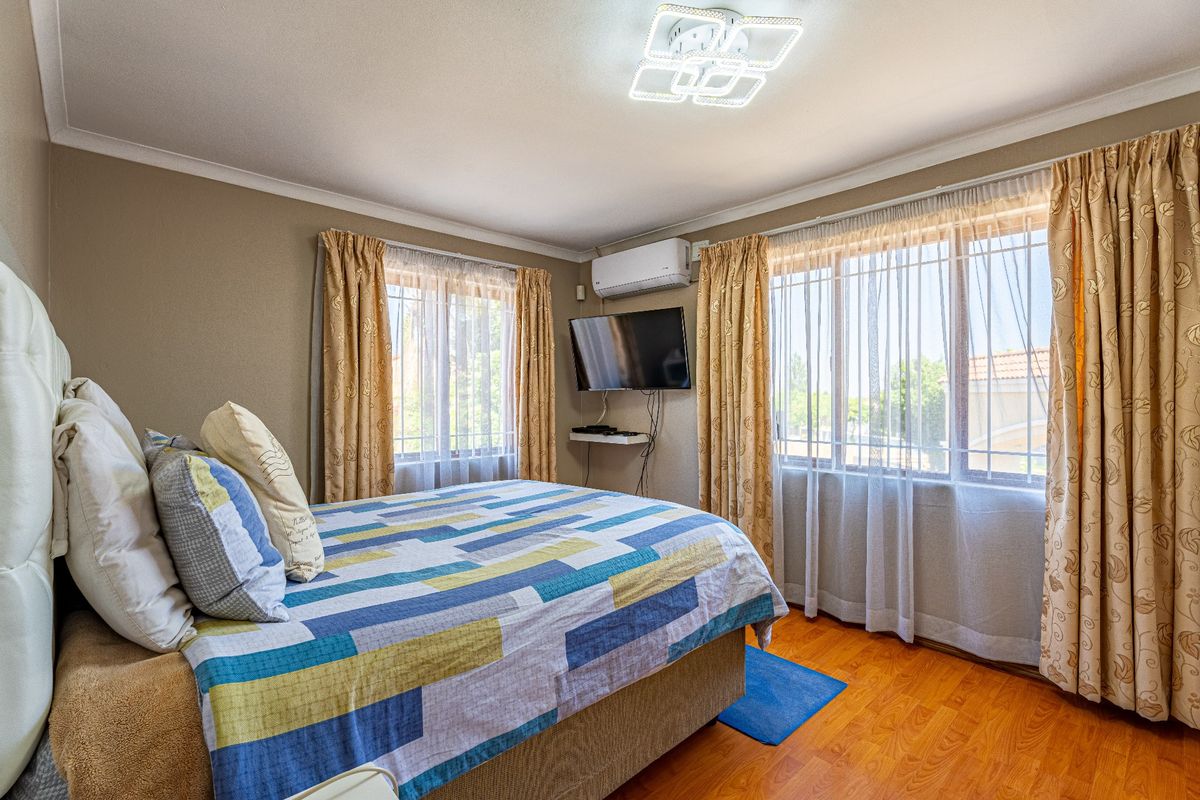 A well-maintained bedroom featuring laminate flooring, an integrated air conditioning unit, and large windows with curtain rails, providing a comfortable living space.