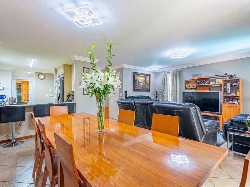 Spacious open-plan living and dining area featuring tiled floors, crown molding, and a seamless transition to the kitchen with a breakfast bar.