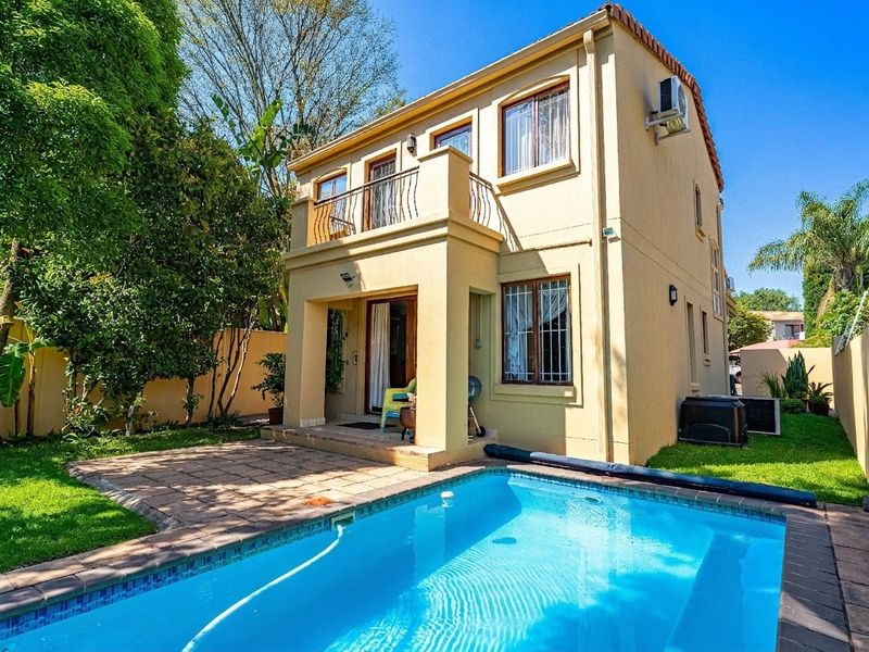 Rear view of the property featuring a swimming pool, paved patio area, and an upper-level balcony with wrought iron railings.
