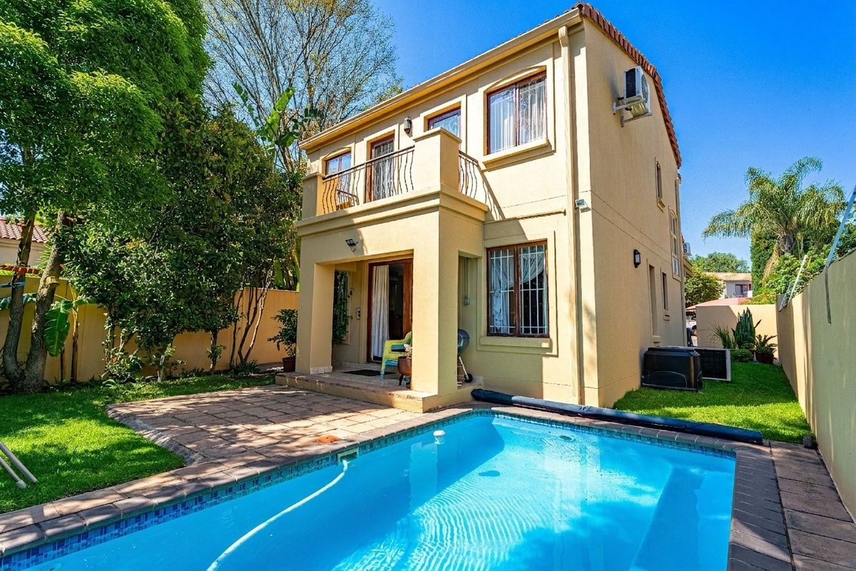 Rear view of the property featuring a swimming pool, paved patio area, and an upper-level balcony with wrought iron railings.