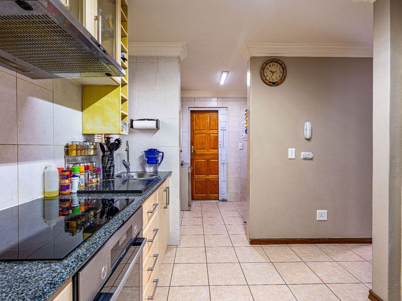 A functional kitchen featuring granite countertops, built-in oven and hob, extractor fan, and tiled flooring, leading to a separate utility area.