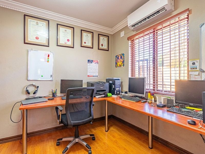 A functional home office featuring laminate flooring, crown molding, and a wall-mounted split-system air conditioner, providing a comfortable workspace.