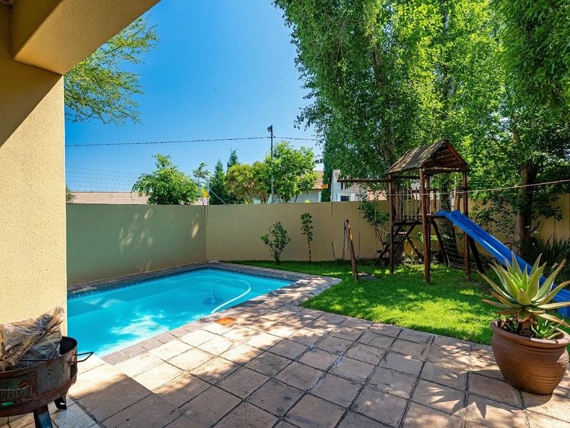 A private backyard featuring a swimming pool, paved patio area, and a well-maintained lawn enclosed by a boundary wall.