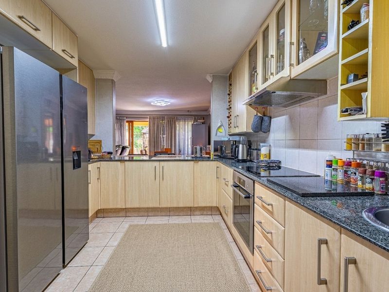 Functional kitchen featuring light wood cabinetry, granite countertops, built-in oven, and hob, with a seamless flow into the adjacent living area.