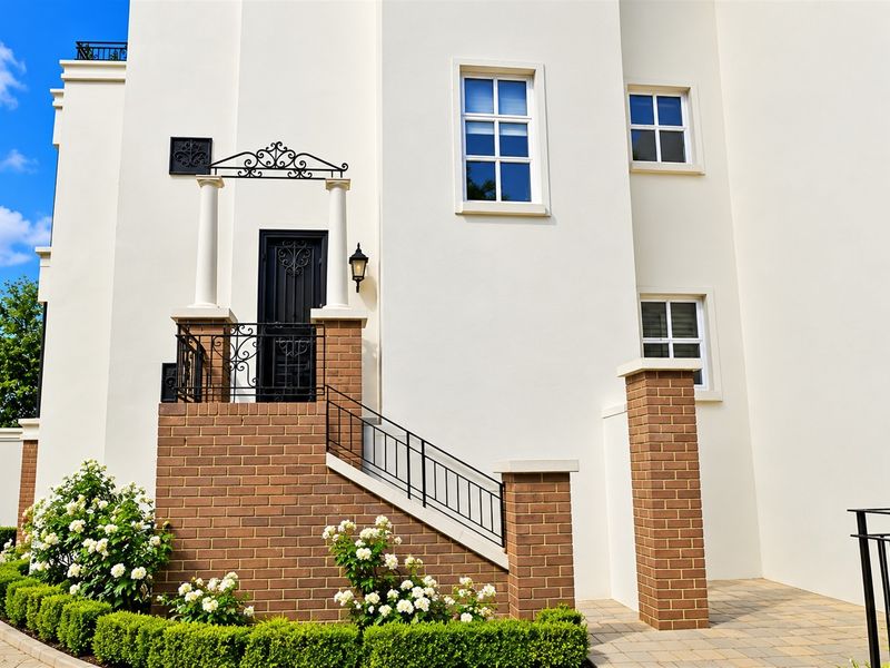 A well-maintained front entrance featuring a brick staircase, wrought iron security door, decorative columns, and manicured garden landscaping.