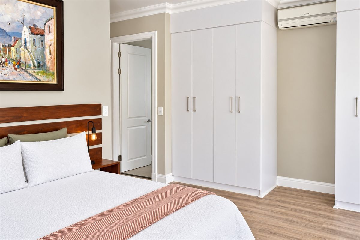 A well-maintained bedroom featuring built-in cupboards, laminate flooring, and a wall-mounted air conditioning unit.