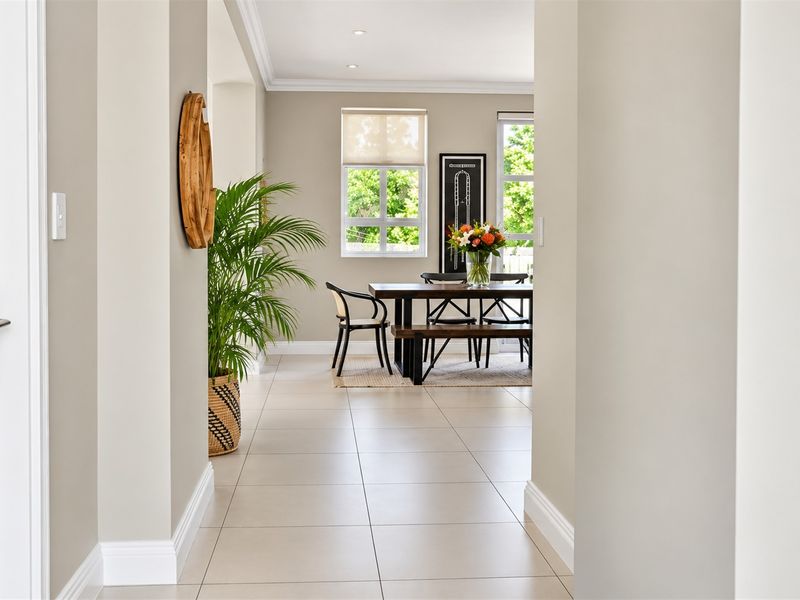 A bright and well-maintained dining area featuring neutral tiled flooring, recessed lighting, and large windows with fitted blinds, creating a clean and inviting space.