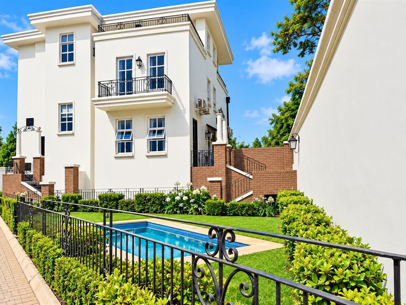 A well-maintained rear exterior view of the apartment building featuring a private swimming pool, landscaped garden, and a balcony with wrought iron railings.
