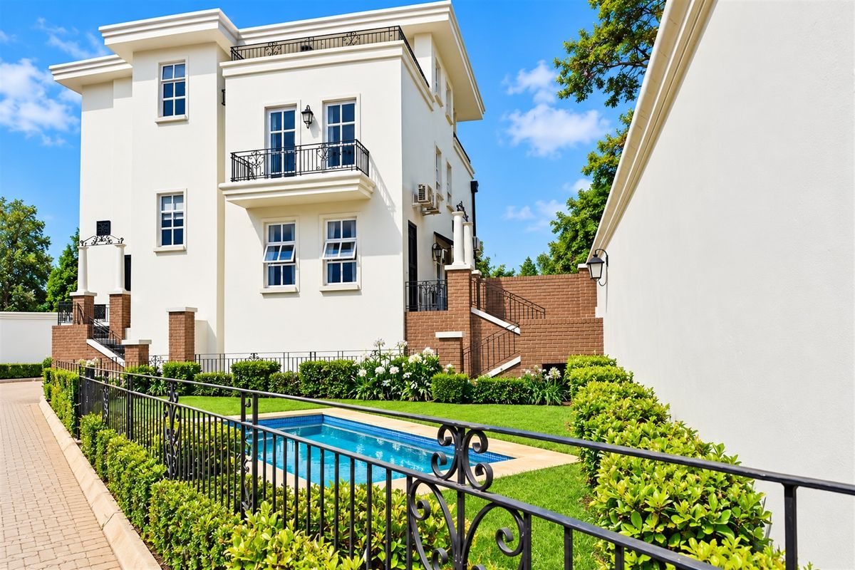 A well-maintained rear exterior view of the apartment building featuring a private swimming pool, landscaped garden, and a balcony with wrought iron railings.