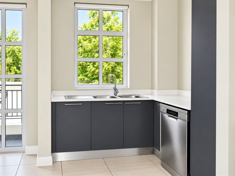 Modern kitchen area featuring dark grey cabinetry, white stone countertops, a double bowl stainless steel sink, and an integrated dishwasher.