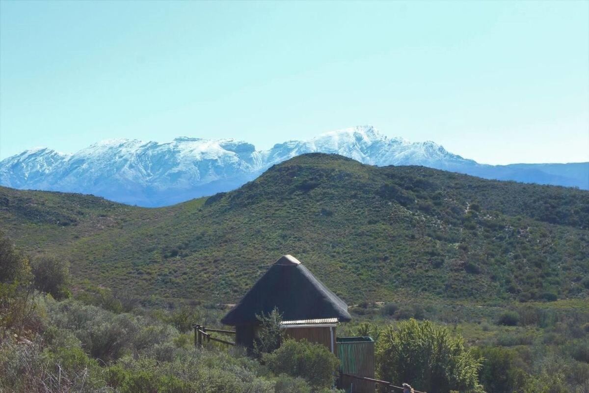 A scenic landscape view featuring a small structure with a traditional thatch roof set against a backdrop of snow-capped mountains.